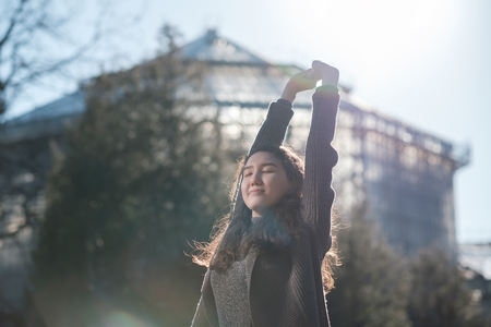 A beautiful Asian girl is standing in the park and resting, basking in the sun. Enjoy the silence in city life.の写真素材