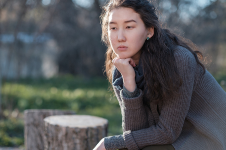 Portrait of an Asian girl in a park. She sits alone and looks sadly away.の写真素材