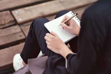The girl is sitting and doing sketches in her notebookの写真素材