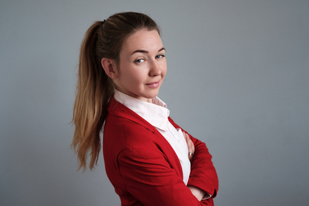 The girl secretary in a red jacket crossed her arms over her chest and turned back a little.の写真素材