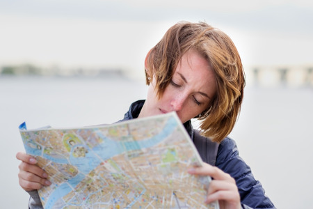 A beautiful girl in a denim jacket is holding a map and trying to understand where she is. Lost in an unfamiliar city. Making a route for the excursion.の写真素材