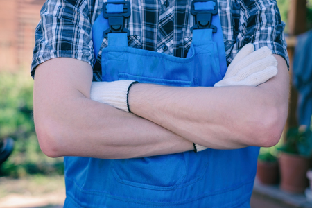 Happy young gardener in overalls with crossed hands