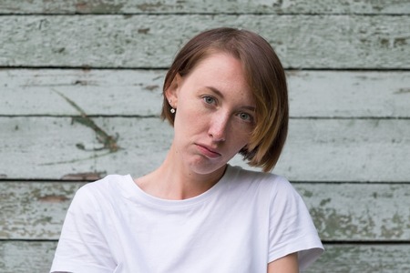 portrait of beautiful young angry woman in white t-shirt on wooden backgroundの写真素材
