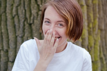 Laughing woman in white shirt with red hair over tree.の写真素材