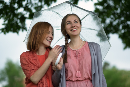 Two women walking park in rain and talk. Friendship and people communication.の写真素材