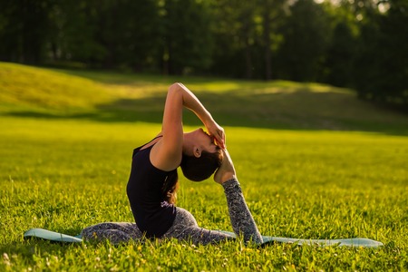 Eka Pada Rajakapotasana pose, on green suuny field in park. Side view