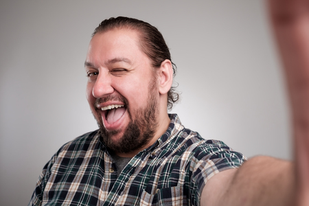 Beautiful young man in casual clothes make selfie on a gray background. He has a happy face, smiling with teeth.の写真素材