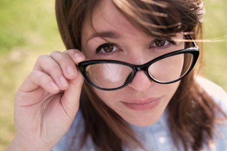 Beautiful young woman adjusting her glasses and smiling at you over blured green nature background.の写真素材