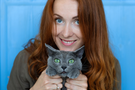 cheerful redhead girl plays with her blue catの写真素材