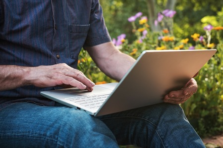 Cropped image of a mature man working on his laptop in garden, old male blogger typing on notebookの写真素材