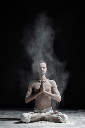 A yoga teacher sits in a sukhasana on a black background.の写真素材