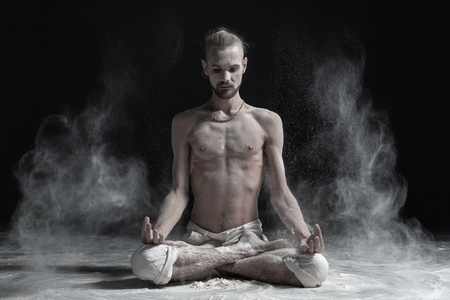 Sporty serene young man meditating sitting in cross-legged yoga lotus pose, Padmasana with palms in mudraの写真素材