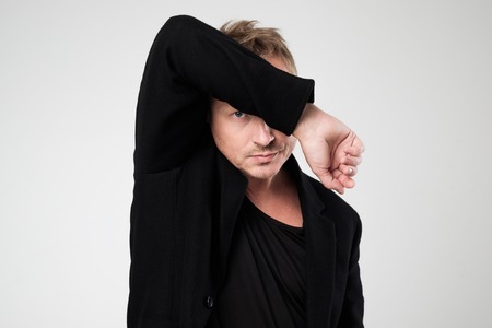 A young man in black clothes looks down in embarrassment. Side view.