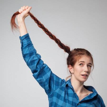 Funny red haired model girl with long braid hair. She holds long braid up.の写真素材