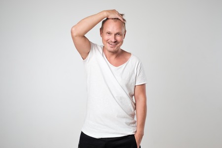 Smiling young man in white t-shirt standing against white background Concept of self confident man.