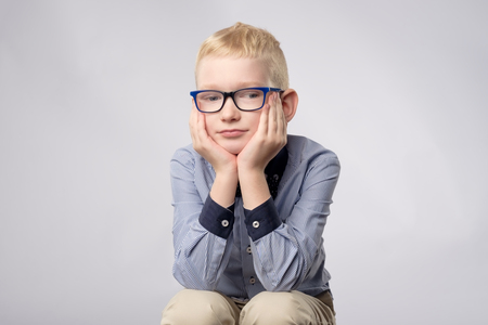 Portrait of caucasian blond boy in glasses looking with bored facial expression to camera on white background.の写真素材