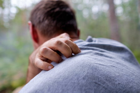 A person sits in the forest and scratches his back from pain or from insect bites.の写真素材
