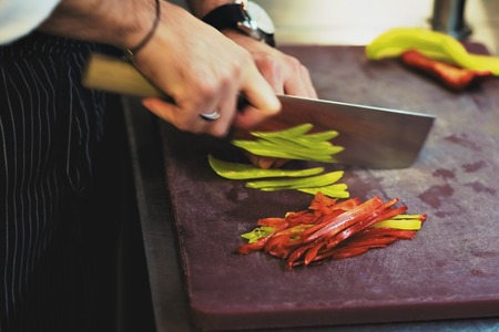 caucasian man is chopping the peppers with a big knife. Cooking in the kitchen of the restaurant.の写真素材