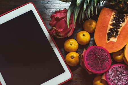 Tropical fruit near modern tablet on wooden background. Vegan lifestyle. Up viewの写真素材