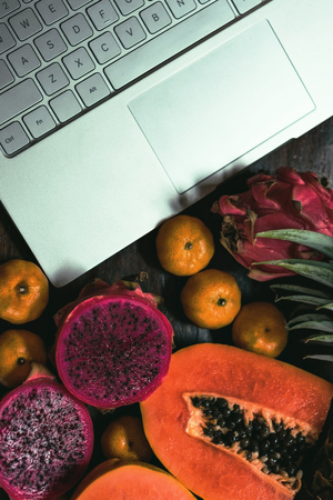 Tropical fruit near modern laptop on wooden background. Vegan lifestyle. Up viewの写真素材