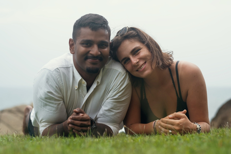 Young romantic mixed race couple lying in park on green grass. Spend free time together on holidaysの写真素材