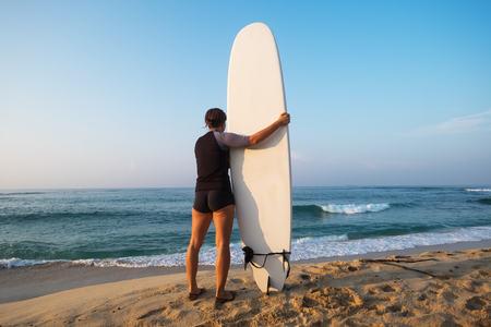 caucasian woman with surfboard standing near water and looking at waves. ready to start surfing