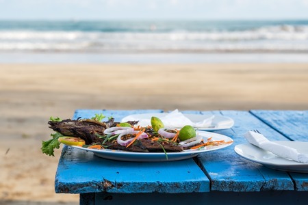 Delicious grilled fish on blue table. Ocean waves on background. Concept of healthy food during vacationの写真素材