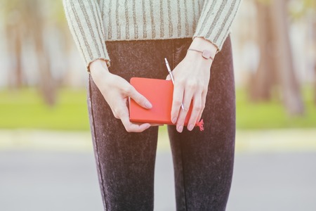 Girl standing outdoor holding a red notebook. Toned effect photoの写真素材
