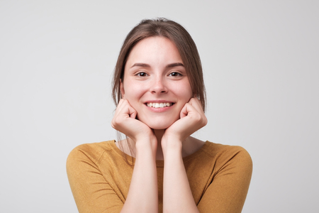 Close up portrait of young happy caucasian woman on white background. She is holding arms near face. Concept of positive facial emotion.の写真素材
