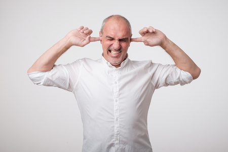 Mature european man closing his ears because of loud sound and noise. I do not want listen to you. Concept of facial negative emotionの写真素材
