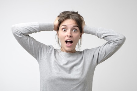 Caucasian woman in simple t-shirt is surprised with nrews holding her head with hands. Concept of news and unexpected results.の写真素材