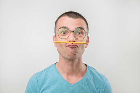 Young european man trying to solve the problem. He is holding pencil between nose and mouth. Concept...