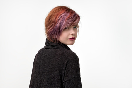 Portrait of unusual informal pretty woman with colorful hairstyle. She is turning back and look...