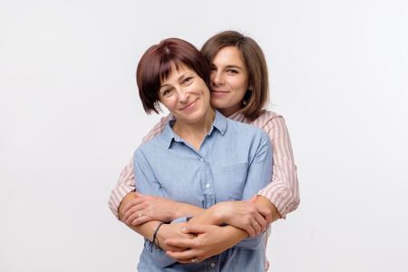 Beautiful maturesenior mom and her adult daughter are hugging, looking at camera and smiling. Good relationships between generations.の写真素材