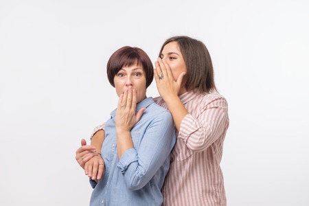 Women mother and daughter gossiping and telling a secret isolated over gray backgroundの写真素材
