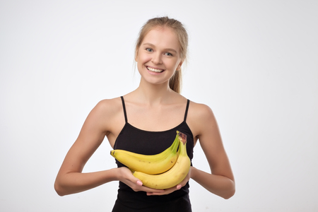 Pretty european blonde woman holding several bananas in her hands and smiling. Concept of healthy fruit dietの写真素材