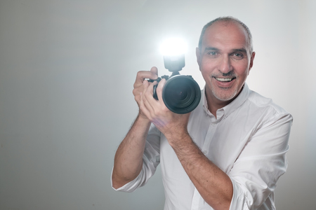Studio shot of ymature spanish man with camera against grey background. Experienced photographer in...