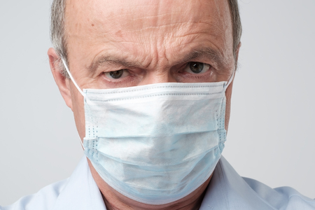 Close up portrait of serious man in special medic mask. He is looking serious. Mature experienced doctor. Medicine, healthcare and emergency in hospitalの写真素材