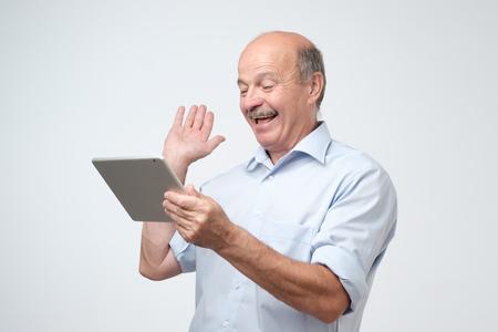 Working on tablet computer. Cheerful mature european man chatting with his friends online.の写真素材