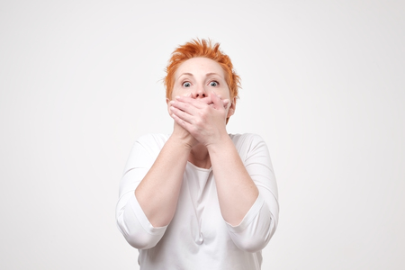 Mature amazed woman covering her mouth with hand on gray background. I wiil not tell this secret anybody. Conspiracy and mystery conceptの写真素材