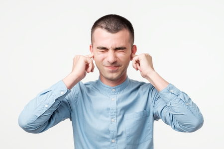 Displeased man plugging ears with fingers. He does not want to listen to arguments. Close up isolated on gray wall backgroundの写真素材