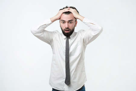 Desperate, stressed young european man looking at camera in terror and shock, holding head, shocked...
