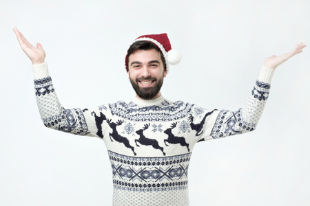 Impressed and surprirsed hispanic man in sweater and christmas hat standing raising hands in amazement and shock reacting to awesome low pricesの写真素材