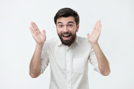 Enthusiastic happy and excited young handsome man raising hands in joy. Positive delighted and surprised facial emotion.の写真素材