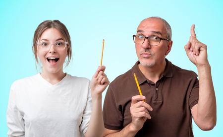 Female caucasian student in glasses and white t-shirt and senior teacher pointing an idea looking very excited standing on bright blue background. Concept of studying in college or universityの写真素材