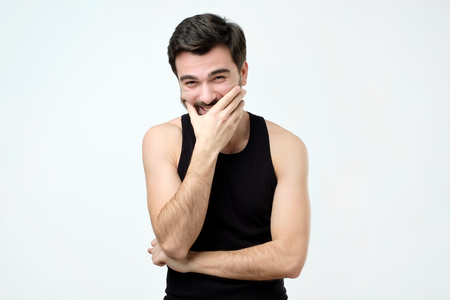 Young man laughing and covering his mouth with hand trying to hold a laugh not to offend some person. He just heard a funny jokeの写真素材