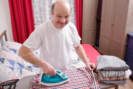 Senior man in whit t-shirt at home ironing his clothes.の写真素材