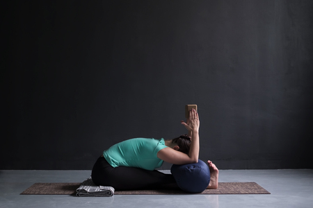 woman practicing yoga, Seated forward bend pose, using block and bolsterの写真素材