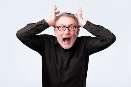 senior man eyes mouth wide open, hands in air yelling screaming shoutingの写真素材