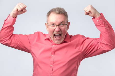 Happy senior handsome man in red shirt and glasses gesturing and keeping mouth. He is happy and celebrating his success.の写真素材